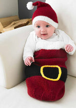 Load image into Gallery viewer, Super cute baby cocoon in a Santa inspired design. Knitted in dark red yarn with a white top. There is a black belt and gold buckle around the centre of the cocoon. The baby is wearing a white banded, dark red Santa hat with white pom pom

