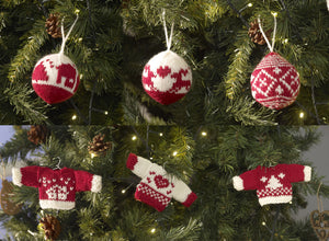 A selection of Xmas tree ornaments knitted in red and white yarn. There are 3 mini Christmas jumpers on hangers. They have a tree, heart or house motif and have contrasting cuffs and band. The 3 baubles have reindeer, houses or geometric shapes 