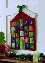 Load image into Gallery viewer, Crocheted advent calendar. Basic shape is a red house with white roof. 3 holly leaves and berries are attached to the point of the roof. Pocket 24 is the door. The other square pockets are a range of colours with gold numbers arranged in columns
