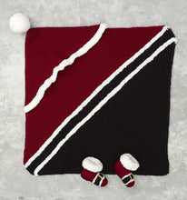 Load image into Gallery viewer, Baby bootees modelled on Santa boots, with buckle and white fur trim. The blanket is knitted diagonally. Half is black with 2 rows of white fur across the centre. Half is red with a 2nd white fur trimmed section attached for the hood with a pompom

