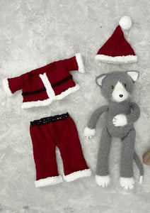 Santa Claws knitted in grey yarn with white paws, nose and ears. Also visible is his dark red trousers and jacket, both fur trimmed with a black belt. His hat is also red with a white fur trim and pom pom bobble