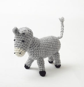 Crocheted donkey in light grey yarn. Its nose is white with 2 black nostril details and black bead eyes. His ears and tail are light grey and his hooves are black