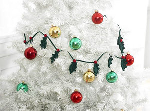 Crocheted holly leaf garland pictured on a white Christmas tree. Each holly leaf is crocheted in dark green DK yarn and attached to the matching cord with a red berry