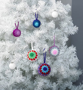White Christmas tree with colourful crocheted bauble decorations. 3 have a coloured centre and then Granny square-like rows. The smaller ones have a multi-pointed star centre and two contrasting coloured rows