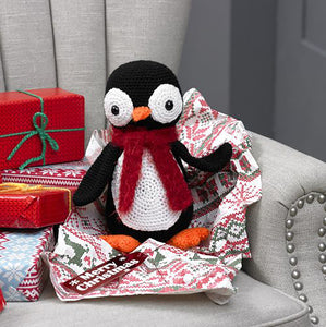 Crocheted penguin toy with large white eyes with black bead centres. It has an orange beak and feet. Its stomach is a large white circle. With black wings, the penguin is finished with a fluffy red scarf