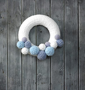 Beautiful icy effect wreath. The main ring is covered in a white chenille like yarn and around the bottom are a selection of pom poms and crocheted balls in different sizes and a mix of lilac, light blue, dusky blue and white