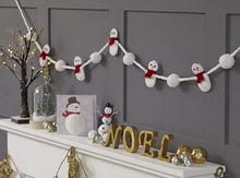 Load image into Gallery viewer, Simple but fun and effective crocheted snowman garland. The hanging cord is white and the snowmen are attached as if the cord is their arms. They are alternated with which pompoms. The snowmen wear red scarves and have black eyes and an orange nose
