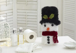 A snowman toilet roll cover knitted in white tinsel yarn with a black tinsel hat. 2 green DK yarn holly leaves and red berry are at the front of the hat. He has an orange nose and dark red scarf. His eyes are black buttons with 3 more down the front